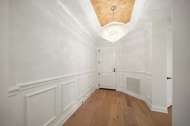 hall with crown molding, visible vents, a decorative wall, wood finished floors, and a chandelier