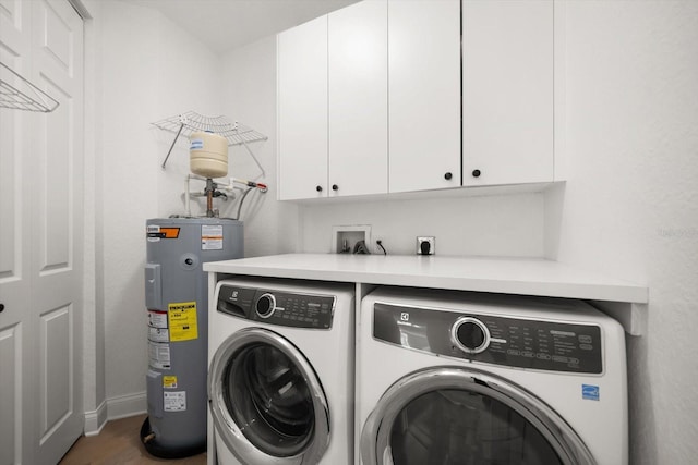 clothes washing area featuring electric water heater, washing machine and dryer, and cabinet space