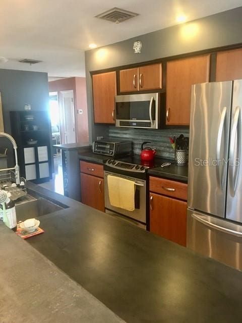 kitchen with visible vents, brown cabinetry, dark countertops, stainless steel appliances, and a sink