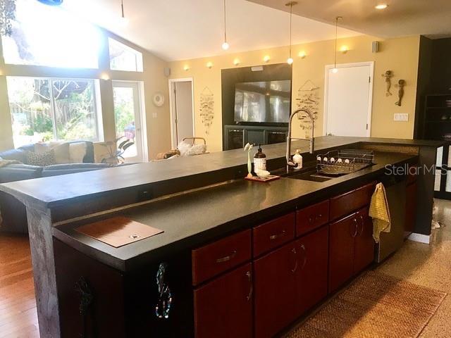 kitchen with a kitchen island, a sink, open floor plan, vaulted ceiling, and dark countertops