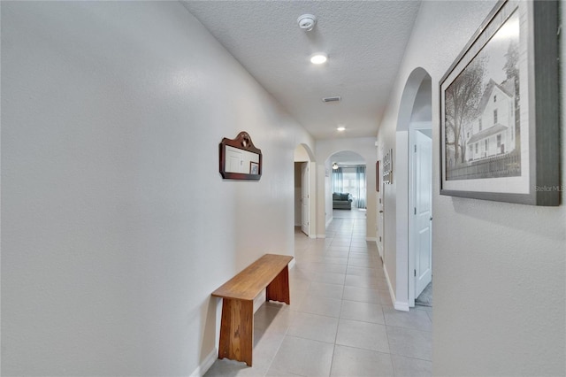 corridor with arched walkways, light tile patterned flooring, a textured ceiling, and baseboards