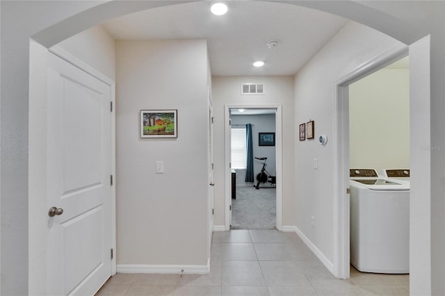 hallway featuring arched walkways, washer and clothes dryer, visible vents, light tile patterned flooring, and baseboards