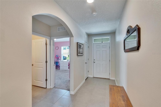 entrance foyer with arched walkways, visible vents, light tile patterned flooring, a textured ceiling, and baseboards