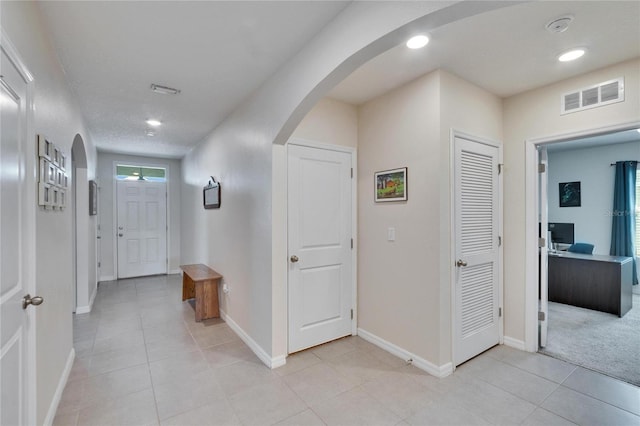 corridor with arched walkways, visible vents, baseboards, and light tile patterned flooring