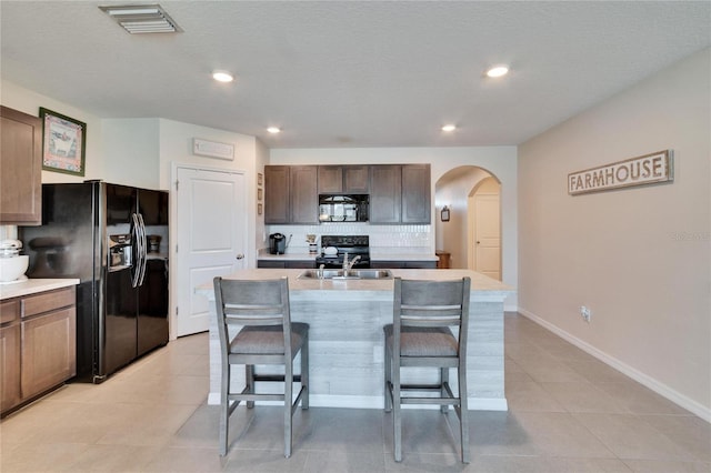 kitchen with light tile patterned floors, tasteful backsplash, visible vents, black appliances, and a sink