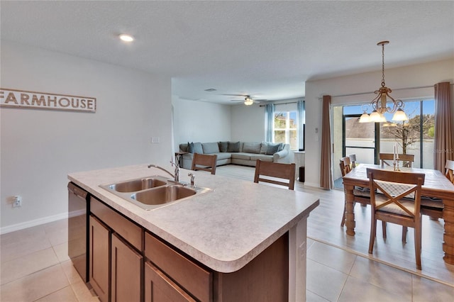 kitchen with decorative light fixtures, a center island with sink, light countertops, a sink, and dishwasher