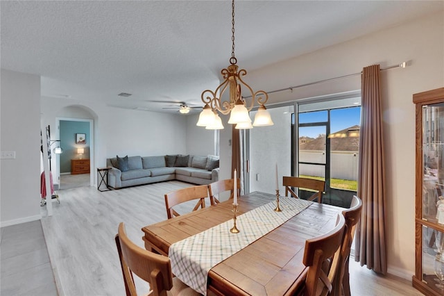 dining space featuring arched walkways, a textured ceiling, visible vents, baseboards, and light wood-style floors