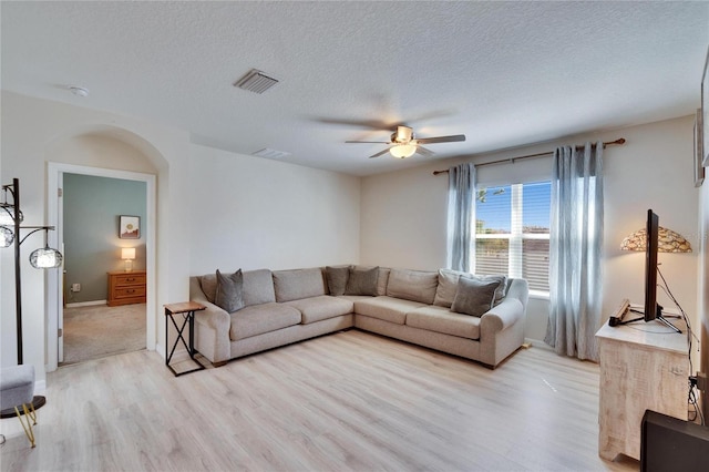 living area featuring light wood-style floors, ceiling fan, visible vents, and arched walkways