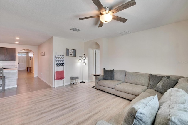 living area featuring arched walkways, light wood-style flooring, a ceiling fan, visible vents, and baseboards