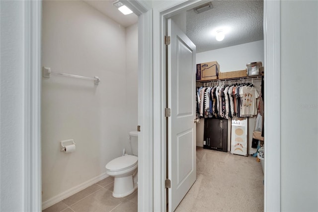 bathroom with visible vents, toilet, tile patterned floors, a spacious closet, and a textured ceiling