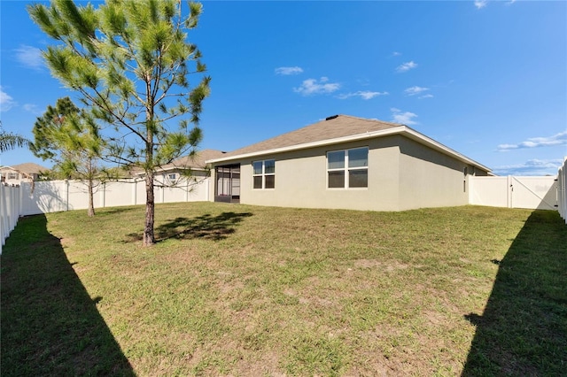 rear view of house featuring a lawn, a fenced backyard, a gate, and stucco siding