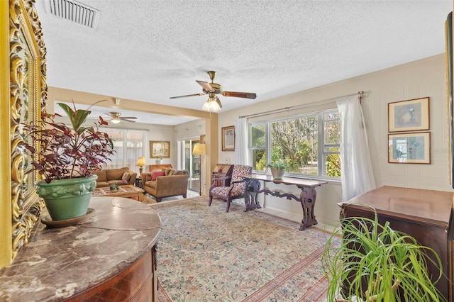 living room featuring a ceiling fan, visible vents, and a textured ceiling