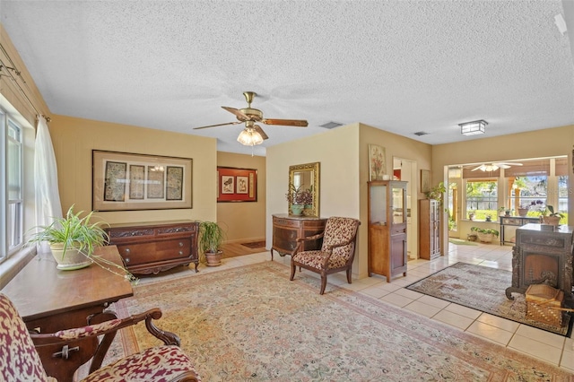 living area featuring tile patterned flooring, visible vents, a ceiling fan, and a textured ceiling