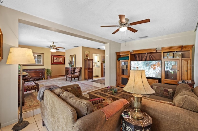 living room featuring light tile patterned floors, ceiling fan, visible vents, and a textured ceiling