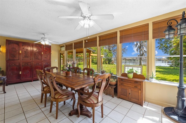 dining space featuring light tile patterned floors, a textured ceiling, a water view, and a ceiling fan