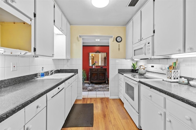 kitchen with dark countertops, white appliances, visible vents, and a sink