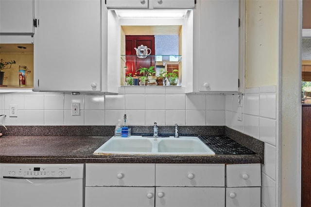 kitchen with tasteful backsplash, dark countertops, white cabinets, white dishwasher, and a sink