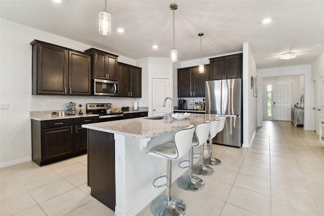 kitchen with dark brown cabinetry, appliances with stainless steel finishes, a kitchen bar, a sink, and light tile patterned flooring