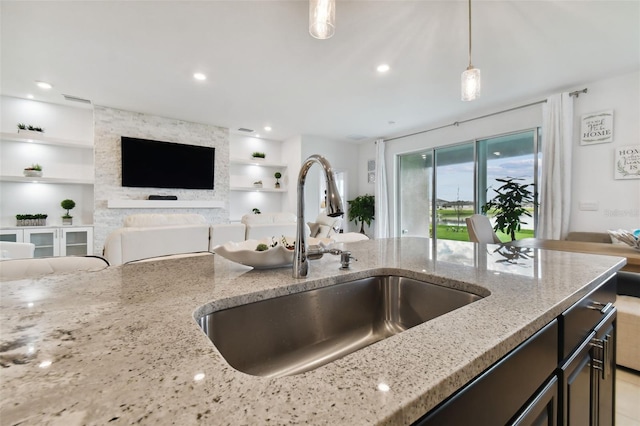 kitchen with built in features, light stone counters, open floor plan, decorative light fixtures, and a sink