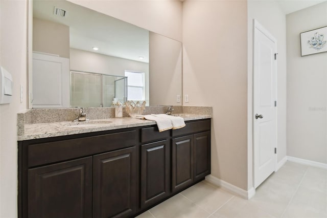 full bath with double vanity, a stall shower, a sink, baseboards, and tile patterned floors