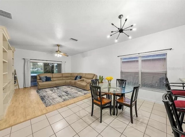 dining area featuring light tile patterned floors, visible vents, and ceiling fan with notable chandelier