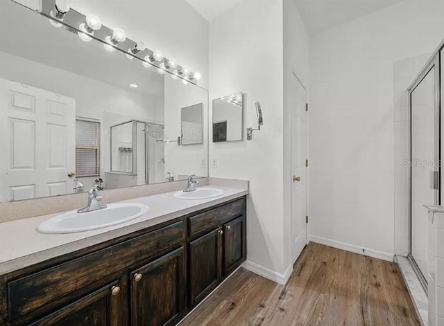 full bath with double vanity, a shower stall, a sink, and wood finished floors