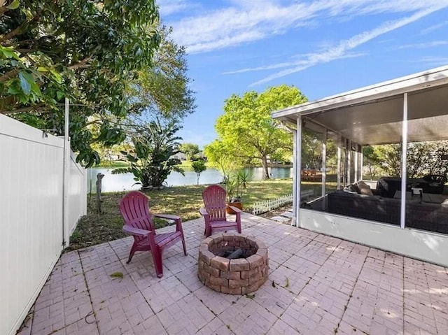 view of patio / terrace featuring a water view, a sunroom, fence, and a fire pit