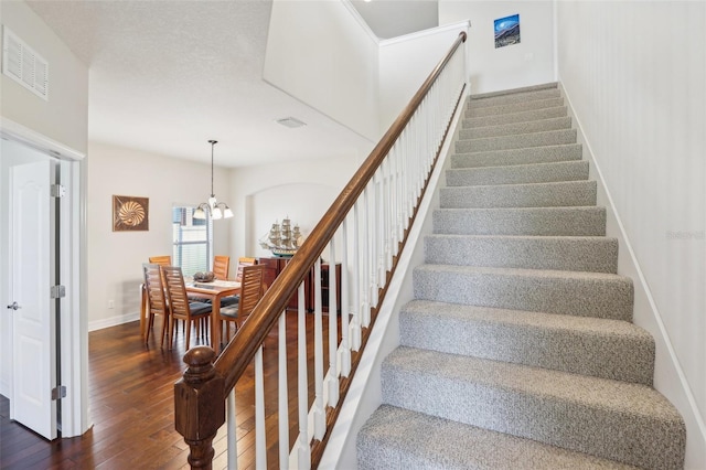 staircase featuring wood-type flooring, visible vents, a chandelier, and baseboards