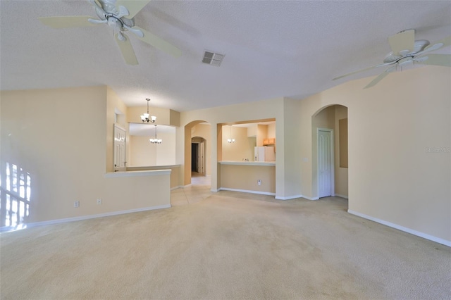 unfurnished living room with arched walkways, ceiling fan with notable chandelier, carpet flooring, and visible vents