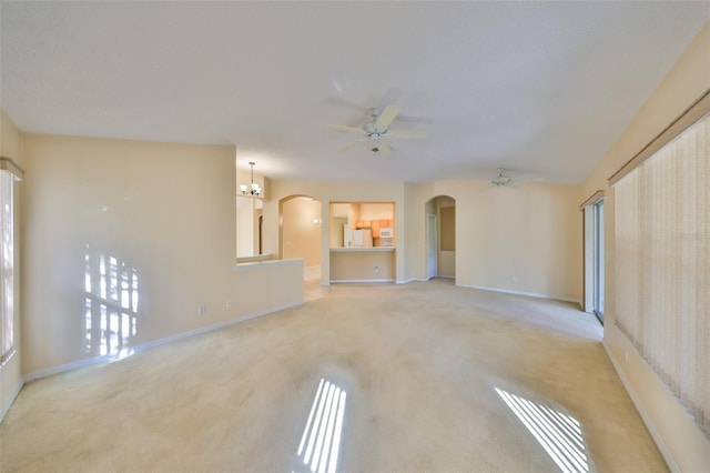 unfurnished living room with arched walkways, ceiling fan, light carpet, and baseboards