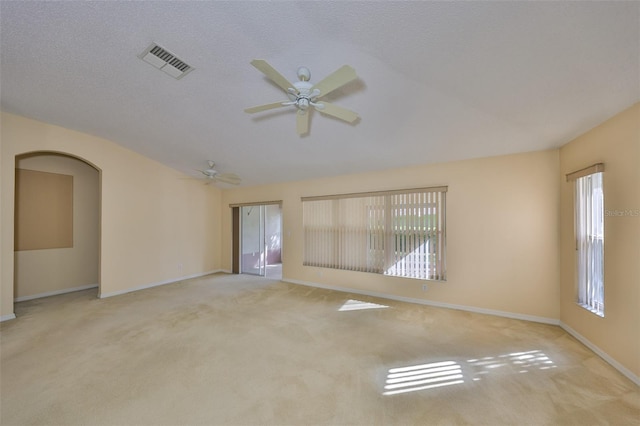 carpeted spare room with lofted ceiling, visible vents, arched walkways, and a wealth of natural light