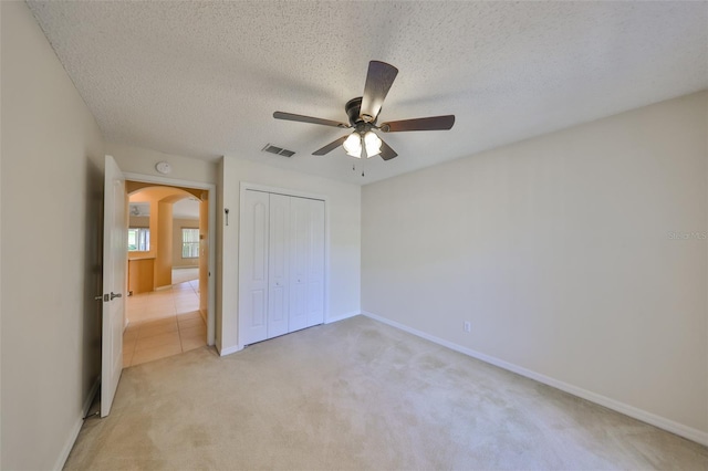 unfurnished bedroom featuring arched walkways, a textured ceiling, light carpet, visible vents, and a closet