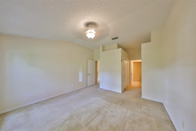 unfurnished bedroom with a textured ceiling, light colored carpet, visible vents, baseboards, and vaulted ceiling