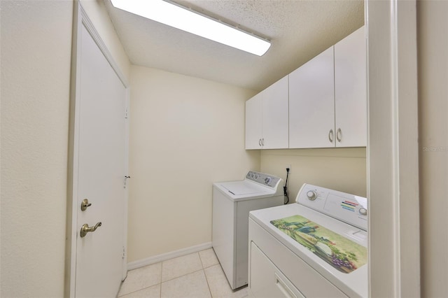 clothes washing area featuring a textured ceiling, light tile patterned flooring, baseboards, washer and dryer, and cabinet space