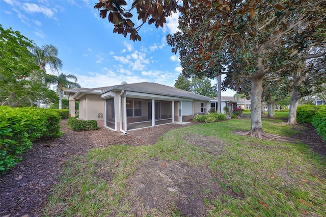 back of property featuring a sunroom, a lawn, and stucco siding