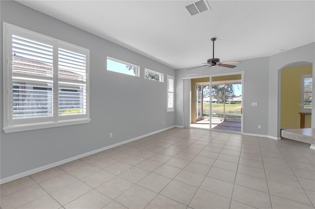 unfurnished room with light tile patterned floors, baseboards, visible vents, arched walkways, and ceiling fan