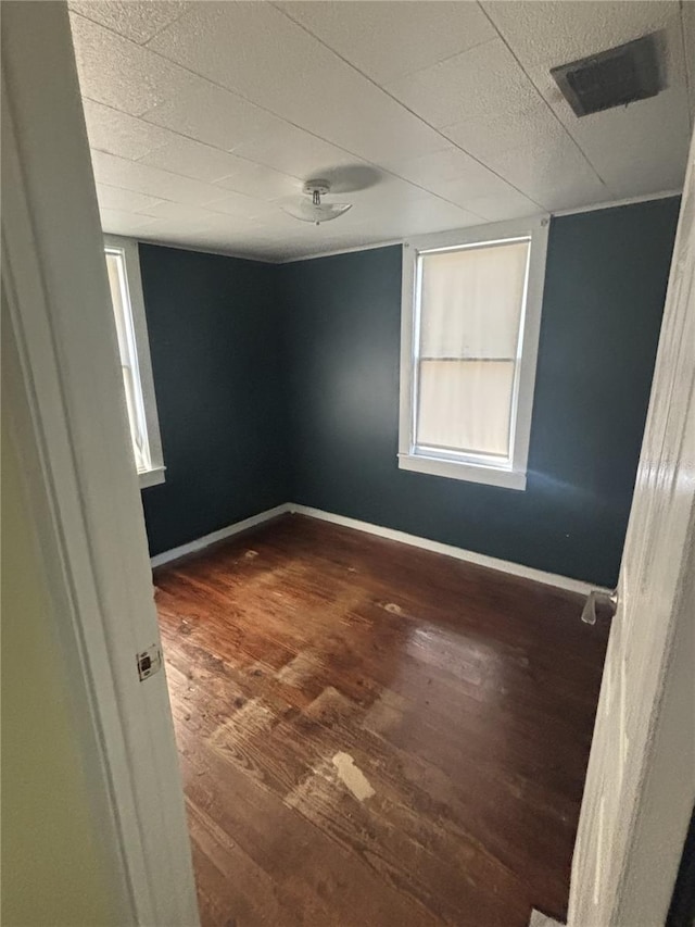 empty room featuring visible vents, a textured ceiling, baseboards, and wood finished floors