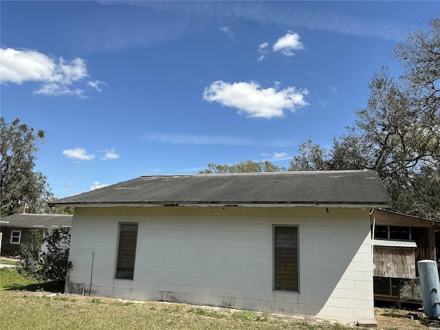 view of side of home with a shingled roof and concrete block siding