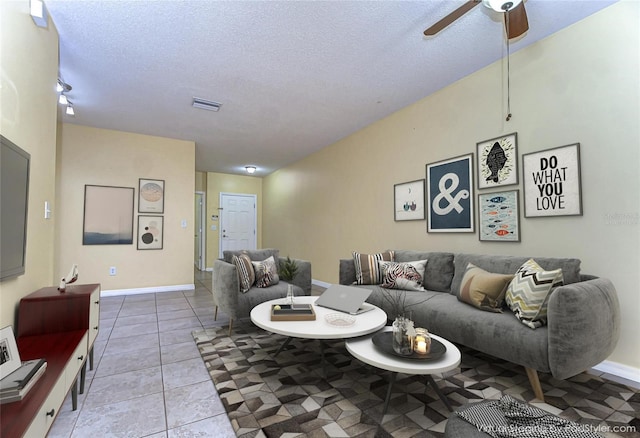 living area featuring light tile patterned floors, visible vents, a ceiling fan, a textured ceiling, and baseboards