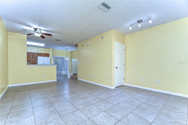 unfurnished room featuring a textured ceiling, light tile patterned floors, visible vents, baseboards, and a ceiling fan