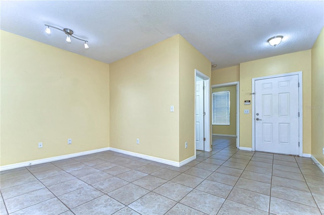 unfurnished room with light tile patterned floors, a textured ceiling, and baseboards