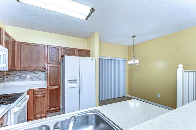 kitchen with tasteful backsplash, light countertops, hanging light fixtures, an inviting chandelier, and white appliances