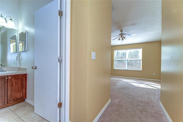 hall featuring light carpet, a textured ceiling, and baseboards