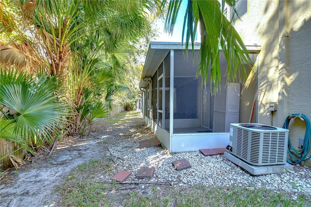 view of side of property featuring stucco siding, fence, a sunroom, and central air condition unit