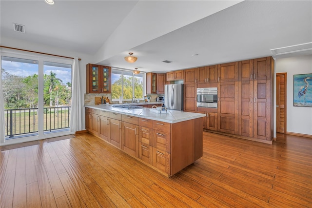 kitchen with a peninsula, visible vents, light countertops, appliances with stainless steel finishes, and glass insert cabinets