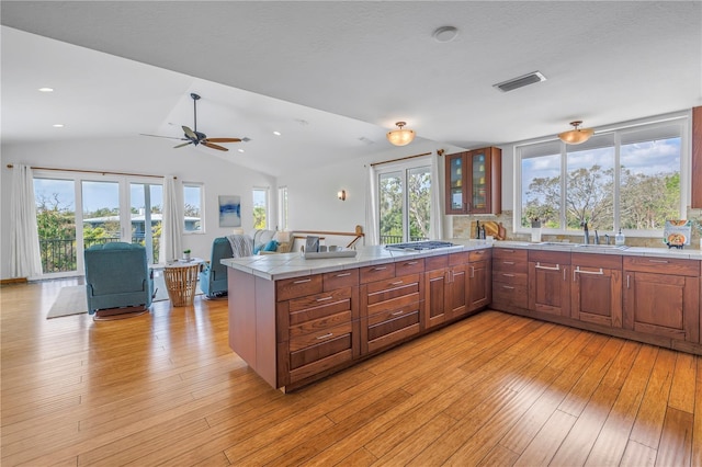 kitchen with visible vents, light wood-style flooring, glass insert cabinets, a peninsula, and a sink