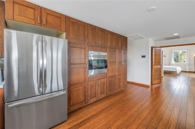 kitchen with stainless steel appliances, wood-type flooring, visible vents, and brown cabinets