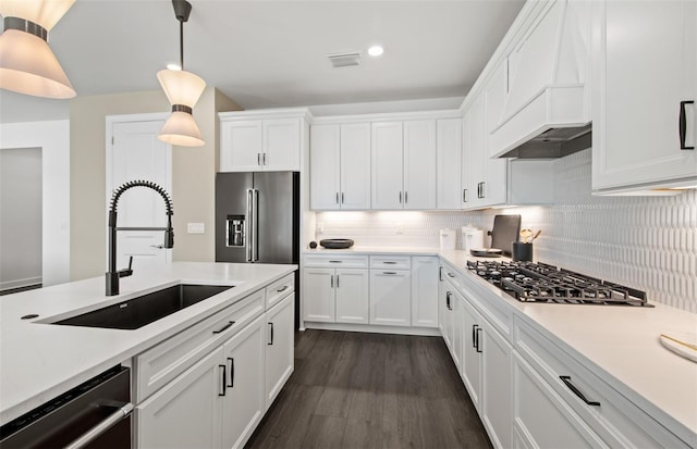 kitchen with tasteful backsplash, appliances with stainless steel finishes, white cabinets, a sink, and premium range hood