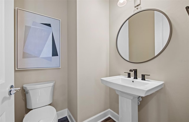 half bath featuring a sink, toilet, and baseboards