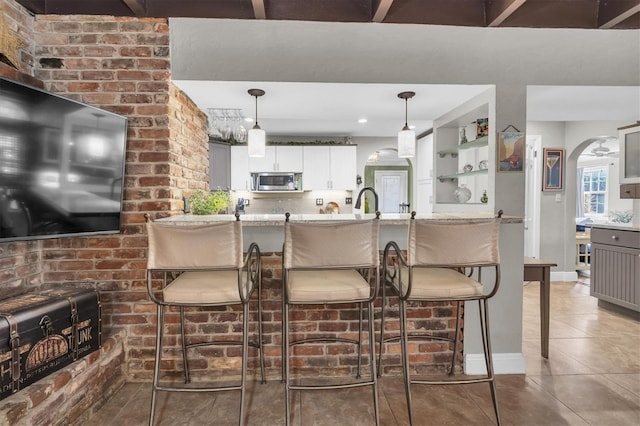 kitchen featuring tile patterned flooring, a kitchen bar, stainless steel microwave, and arched walkways